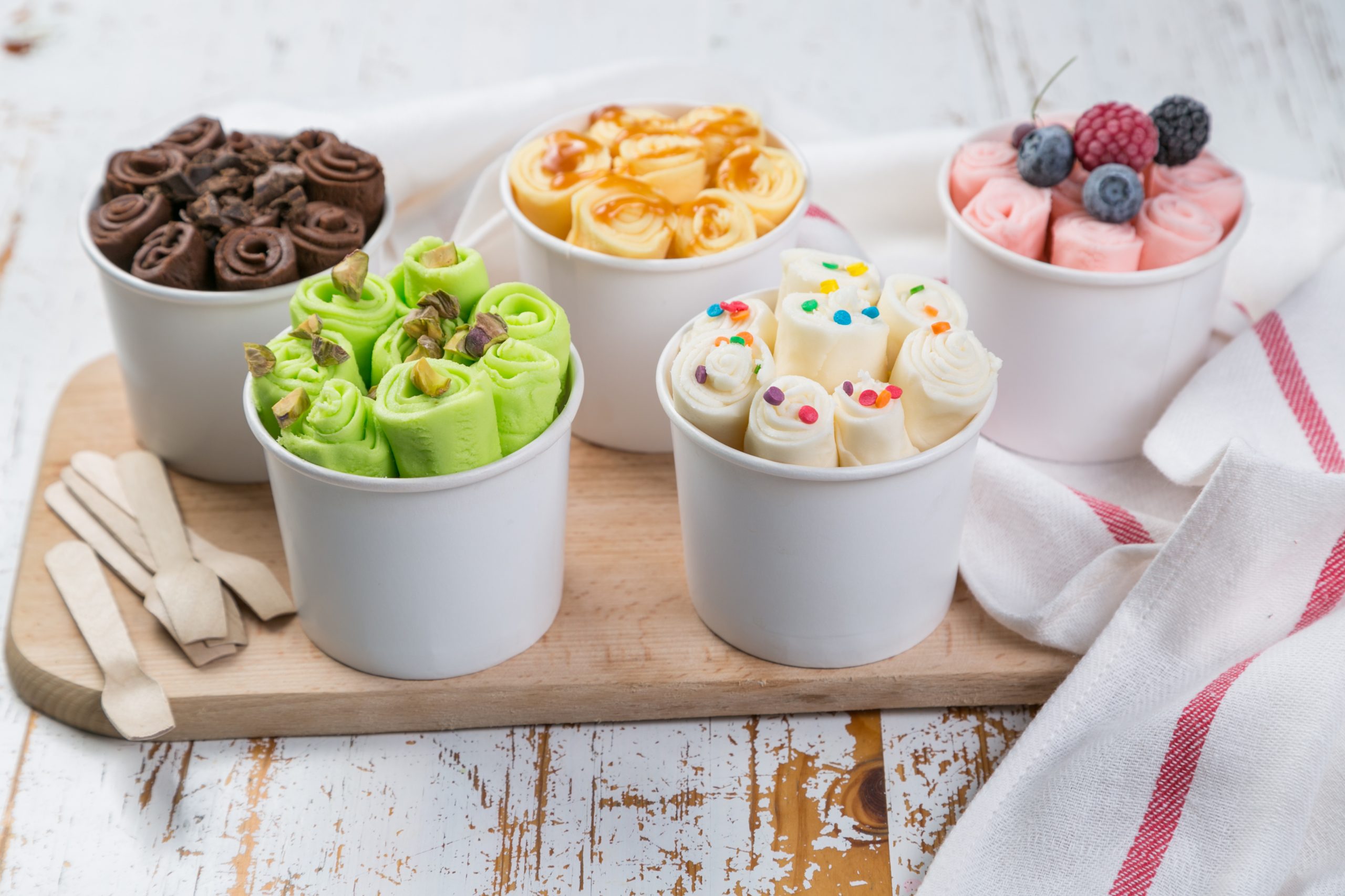 Selection of different rolled ice creams in cone cups, rustic wood background, copy space